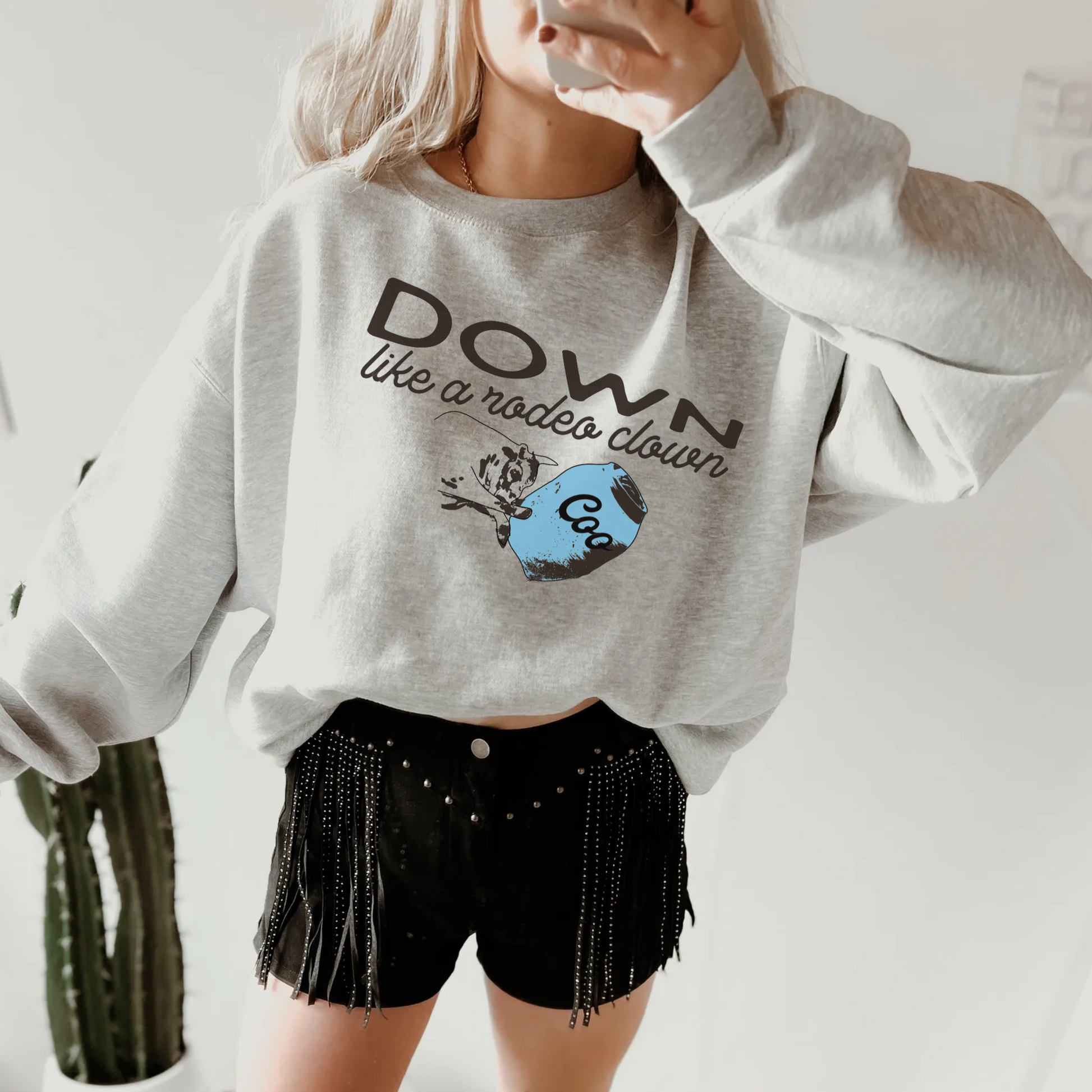 A person wearing a down like a rodeo clown sweatshirt with a rodeo clown and barrel on the front